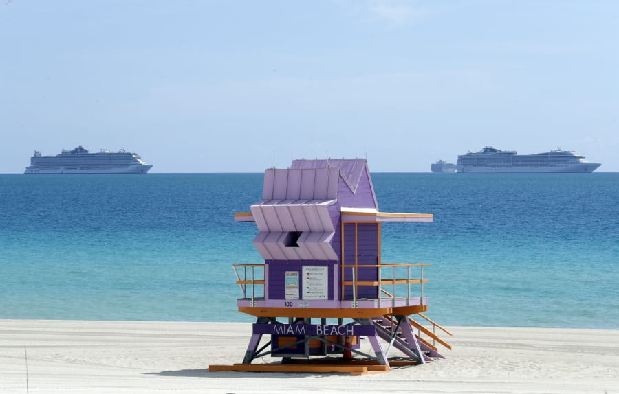 Two cruise ships are anchored offshore past a lifeguard tower, Tuesday, March 31, 2020, in Miami Beach, Fla.