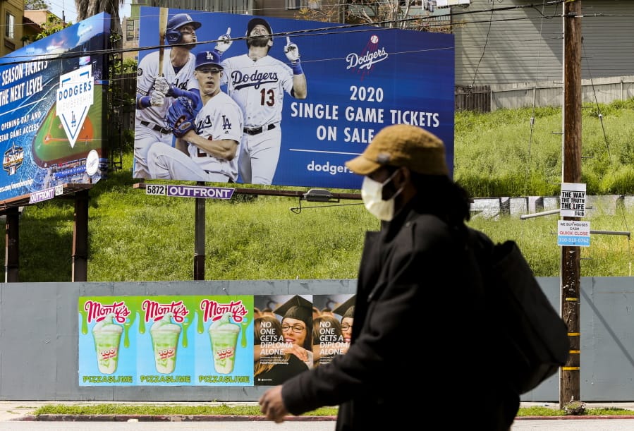 A pedestrian wears a hat and a face mask on Sunset Blvd., in the Echo Park neighborhood of Los Angeles, Thursday, April 2, 2020. Major League Baseball opening day was to have been Thursday, March 26, but was pushed back to mid-May at the earliest because of the coronavirus outbreak. The spring training schedule was cut short on March 12 because on the pandemic, and it remains unclear when and if baseball can resume.