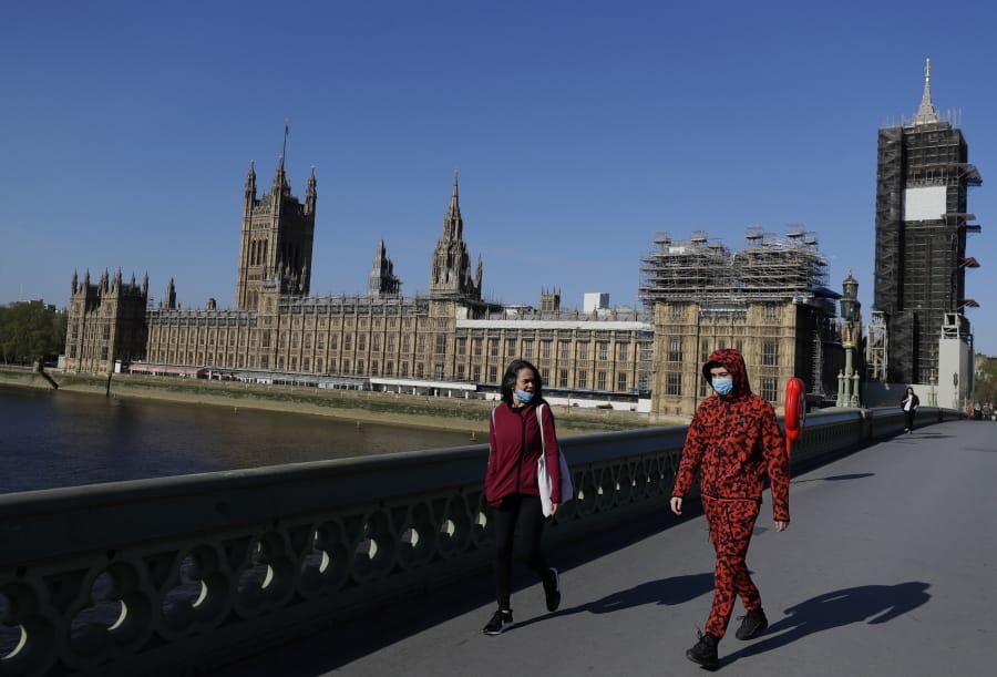 People wear masks as they walk near Britain&#039;s Houses of Parliament as the country is in lockdown to help curb the spread of coronavirus, in London, Tuesday, April 21, 2020. Britain&#039;s Parliament is going back to work, and the political authorities have a message for lawmakers: Stay away. U.K. legislators and most parliamentary staff were sent home in late March as part of a nationwide lockdown to slow the spread of the new coronavirus.