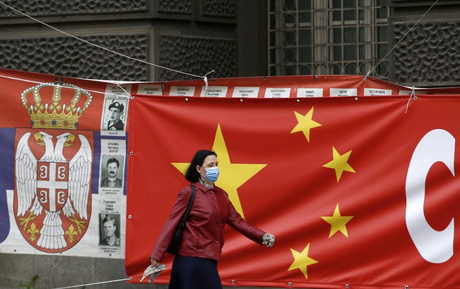 In this April 13, 2020, photo, a woman wearing a face mask walks by a Chinese flag placed on a street prior a curfew set up to limit the spread of the new coronavirus in Belgrade, Serbia.  While China struggles elsewhere to polish its image tarnished by its initial handling of the coronavirus outbreak, Beijing has no problem maintaining its hard-won influence in Eastern Europe, where it battles for clout with the EU as well as with Russia in countries like Serbia.