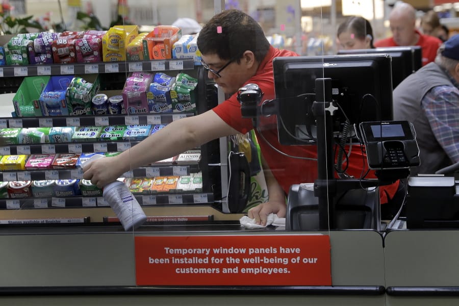 FILE - In this March 26, 2020, file photo, Garrett Ward sprays disinfectant on a conveyor belt between checking out shoppers behind a plexiglass panel at a Hy-Vee grocery store in Overland Park, Kan. From South Africa to Italy to the U.S., grocery workers -- many in low-wage jobs -- are manning the front lines amid worldwide lockdowns, their work deemed essential to keep food and critical goods flowing.