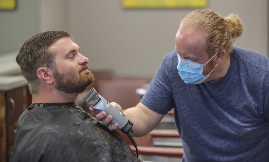 Barber and owner of Chris Edwards wears a mask and cuts the hair of customer David Boswell at Peachtree Battle Barber Shop in Atlanta on Friday, April 24, 2020. The first phase of Georgia Gov. Brian Kemp&#039;s plan to reopen Georgia during the coronavirus pandemic included haircut shops and gyms, though not all chose to open their doors.