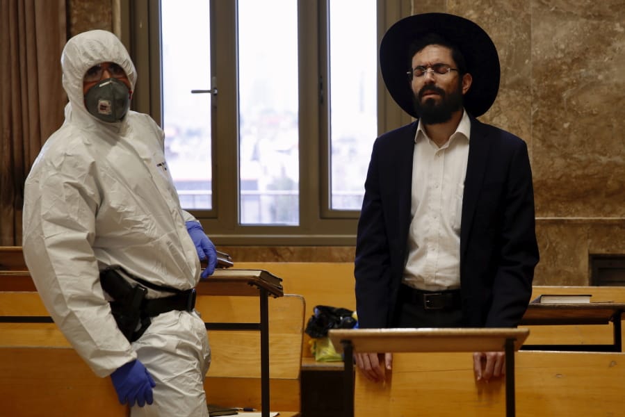 An Israeli police officer wearing protective gear waits to detain an ultra-Orthodox man as he prays in a synagogue because of the government&#039;s measures to help stop the spread of the coronavirus, in Bnei Brak, a suburb of Tel Aviv, Israel, Thursday, April 2, 2020. ?On Wednesday, Israeli Prime Minister Benjamin Netanyahu ordered a police cordon around the largely ultra-Orthodox city of Bnei Brak, to limit movement to and from the city. Bnei Brak has the second highest number of coronavirus cases in Israel.