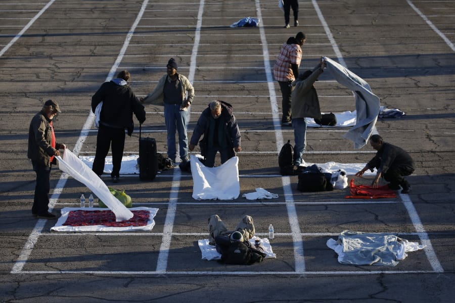 People prepare places to sleep in area marked by painted boxes on the ground of a parking lot at a makeshift camp for the homeless Monday, March 30, 2020, in Las Vegas. Officials opened part of a parking lot as a makeshift homeless shelter after a local shelter closed when a man staying there tested positive for the coronavirus.