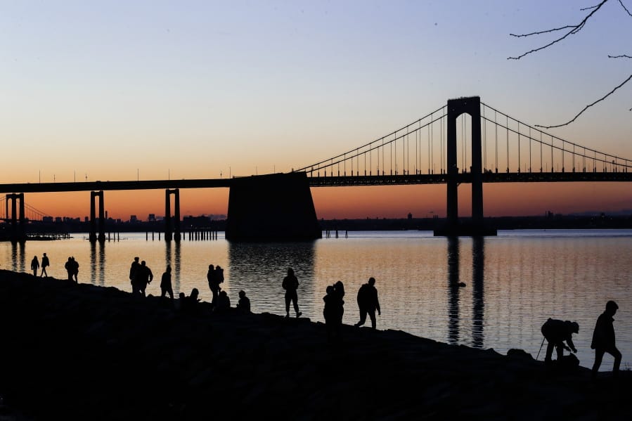 People gather to watch the sun set behind the Throgs Neck Bridge at LIttle Bay Park Wednesday, April 8, 2020, in the Queens borough of New York. While New York Gov. Andrew Cuomo said New York could be reaching a &quot;plateau&quot; in hospitalizations, he warned that gains are dependent on people continuing to practice social distancing.
