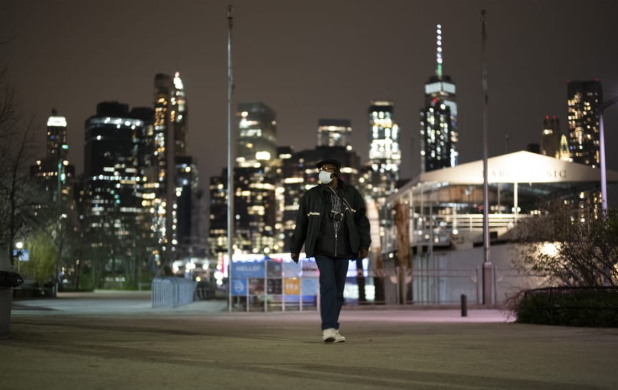 A man wearing a mask walks through Brooklyn Bridge Park, Tuesday night, April 14, 2020 during the coronavirus pandemic in New York. Known as &quot;The City That Never Sleeps,&quot; New York&#039;s streets are particularly empty during the pandemic.