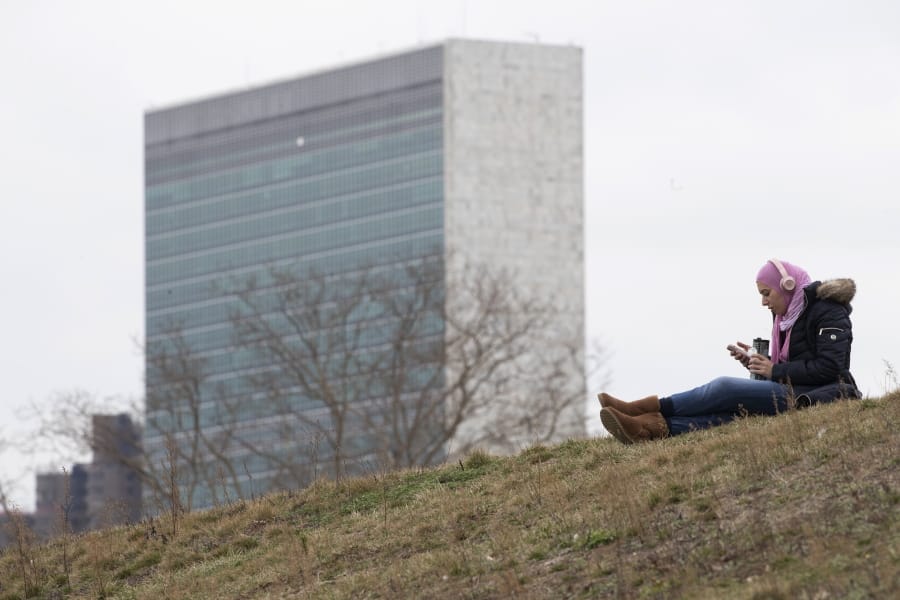 A woman listens to music at a park on Roosevelt Island, Tuesday, March 17, 2020, in New York, with a United Nations building in the background. New York State entered a new phase in the coronavirus pandemic Monday, as New York City closed its public schools, and officials said schools statewide would close by Wednesday. New York joined with Connecticut and New Jersey to close bars, restaurants and movie theaters along with setting limits on social gatherings.