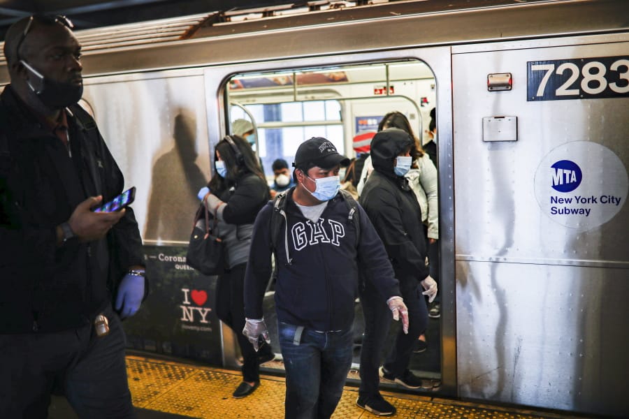 Subway riders, wearing personal protective equipment due to COVID-19 concerns, step off a train, Tuesday, April 7, 2020, in New York. The new coronavirus causes mild or moderate symptoms for most people, but for some, especially older adults and people with existing health problems, it can cause more severe illness or death.