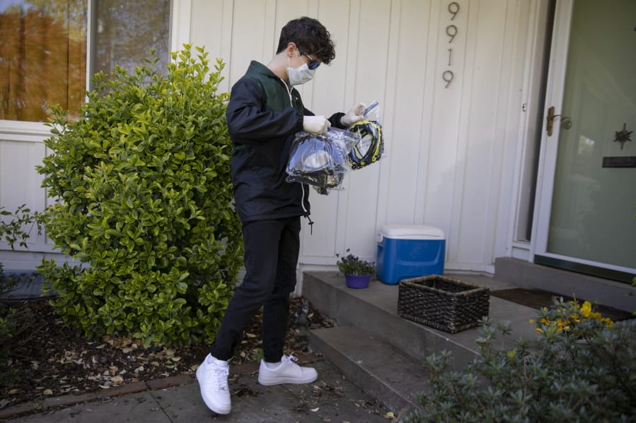 High school junior, Will Olsen, 17, of Kensington, Md., picks up bags holding pieces for medical face shields that were printed using personal 3D printers, in Kensington, Md., Sunday, April 19, 2020. He then delivered the bags to the Eaton Hotel in downtown Washington for assembly.