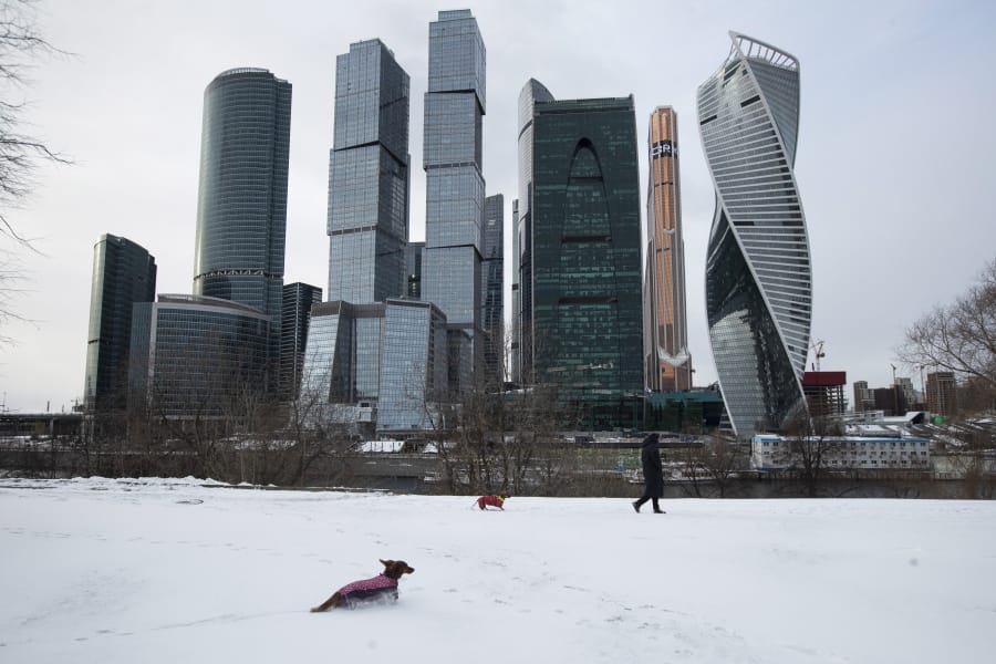 A woman walks her dogs with Moscow City skyscrapers in the background in Moscow, Russia, Tuesday, March 31, 2020. The Russian capital has woken up to a lockdown obliging most people in the city of 13 million to stay home. The government ordered other regions of the vast country to quickly prepare for the same as Moscow, to stem the spread of the new coronavirus. The new coronavirus causes mild or moderate symptoms for most people, but for some, especially older adults and people with existing health problems, it can cause more severe illness or death.