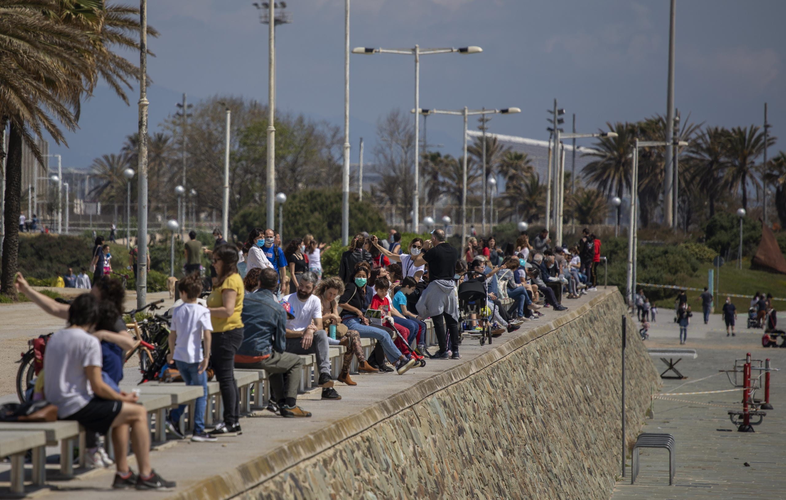 Families with their children sit in a boulevard as police patrol the beach, where access is prohibited, in Barcelona, Spain, Sunday, April 26, 2020 as the lockdown to combat the spread of coronavirus continues. On Sunday, children under 14 years old will be allowed to take walks with a parent for up to one hour and within one kilometer from home, ending six weeks of compete seclusion.