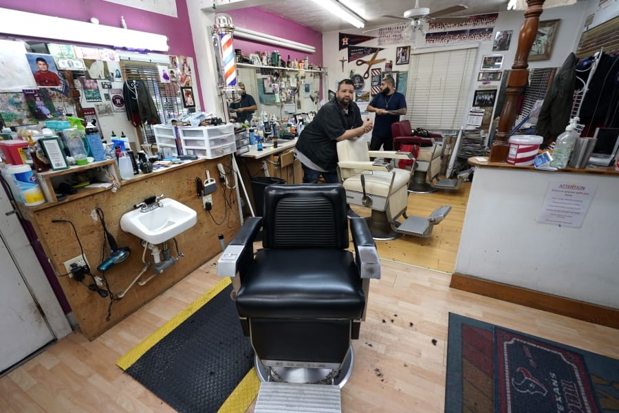 FILE - In this Friday, March 20, 2020 file photo, Carlos Vasquez, left, and his nephew, R.J. Vasquez, wait for customers at their family&#039;s barber shop in Houston. They estimate they have lost nearly half of their business due to the COVID-19 coronavirus. (AP Photo/David J.