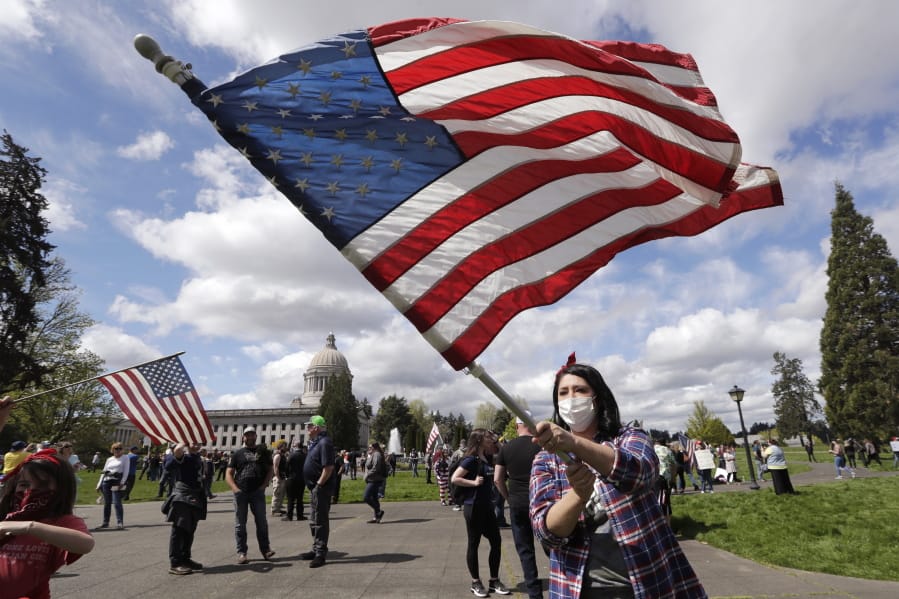 Janell Sorensen of Woodland waves a flag as demonstrators gather at the Capitol in Olympia to oppose Washington&#039;s stay-home order to slow the coronavirus outbreak Sunday. State Rep. Vicki Kraft, R-Vancouver, was also in attendance to support the protest.