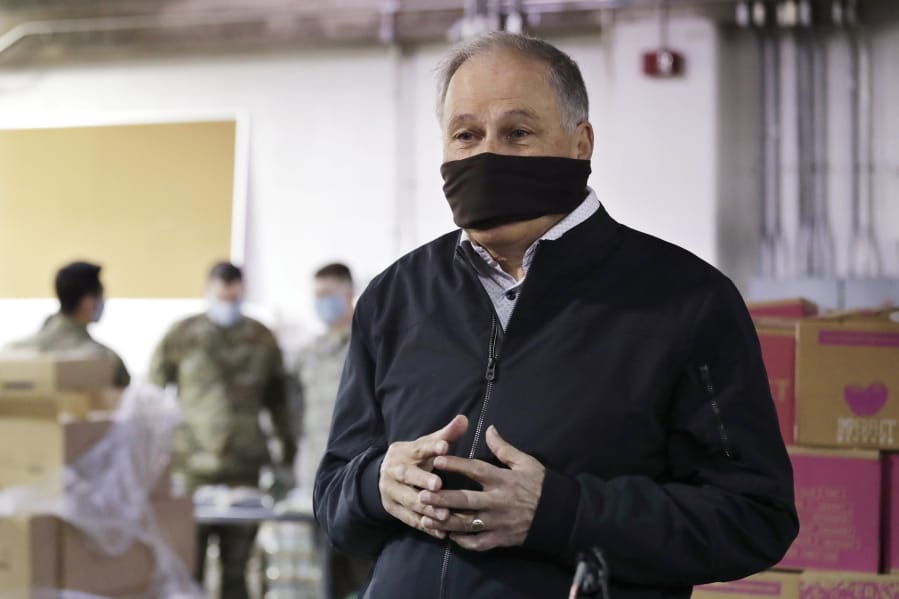 Gov. Jay Inslee wears a makeshift mask as he speaks with media members while visiting inside Nourish Pierce County warehouse, where Washington National Guard members were packing food in response to the coronavirus outbreak Friday in Lakewood.