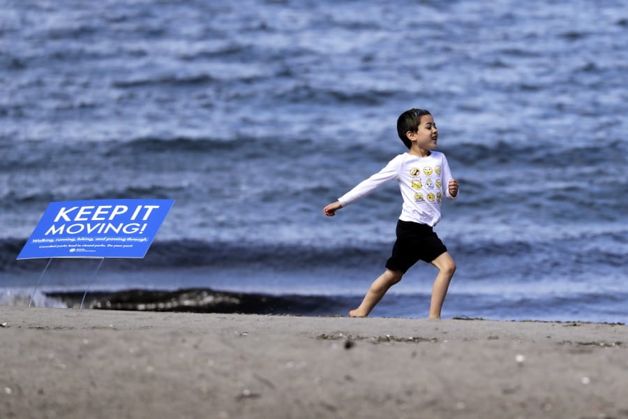 Corliss Roberson, 6, takes the &quot;Keep it moving&quot; sign literally as he races along a beach in a city park Monday, April 27, 2020, in Seattle. City guidelines for Seattle parks ask that people stay at least six feet apart, not to congregate and to keep moving to help prevent spread of the coronavirus.