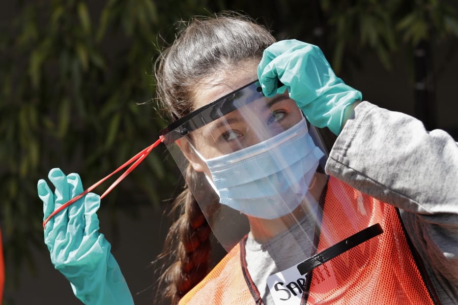 Volunteer Sarah Nishikawa tries on a homemade face shield to see how it works after receiving several shopping bags full of them at a drive-up donation location for medical supplies at the University of Washington to help fight the coronavirus outbreak Tuesday, April 14, 2020, in Seattle.
