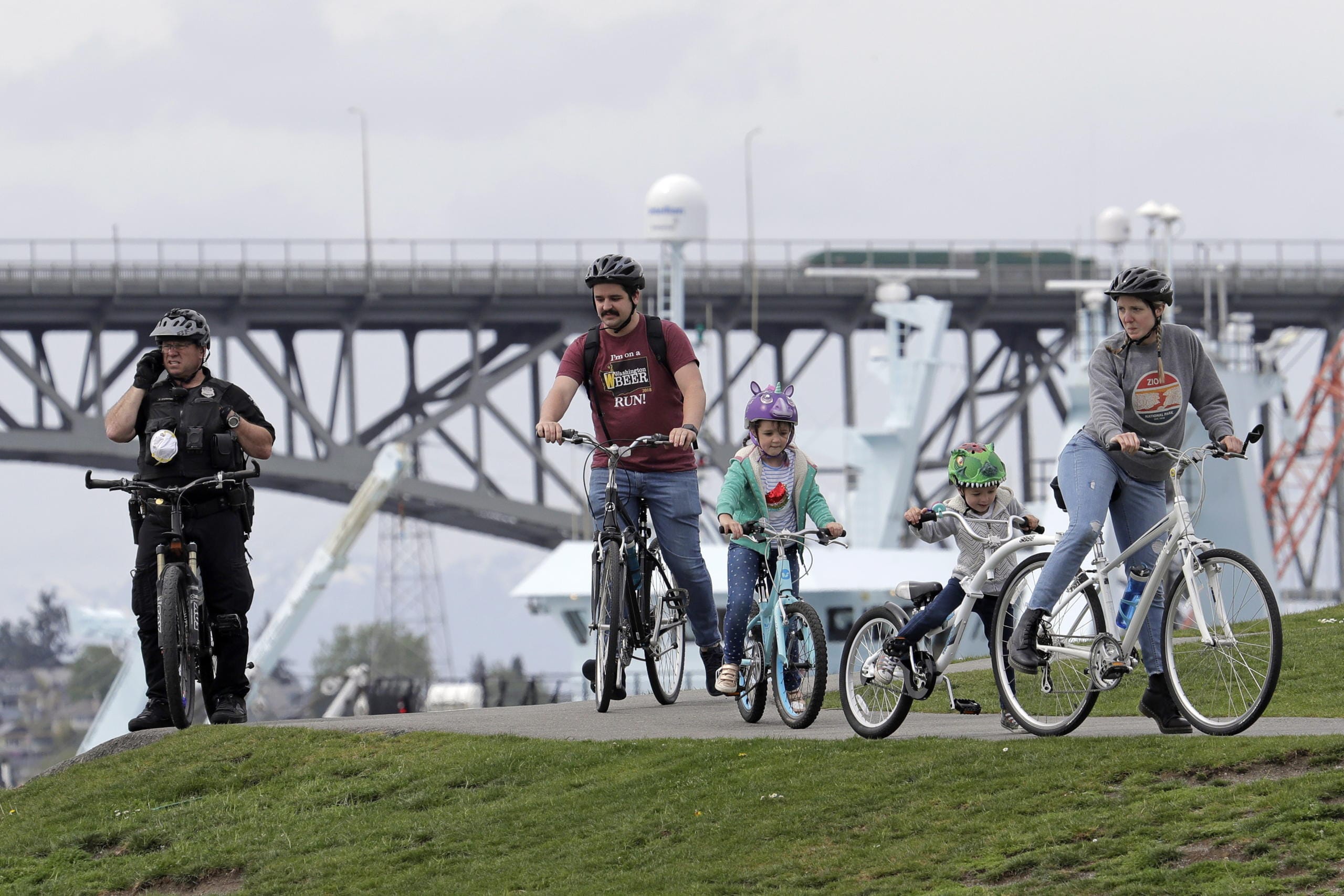 A Seattle Police Officer on a bicycle watches from a hill as people ride by at Gas Works Park in Seattle, Sunday, April 26, 2020. The park and others in Seattle were open Sunday, but officials sought to prevent the spread of the coronavirus by urging people to keep moving and not to gather in large groups. (AP Photo/Ted S.
