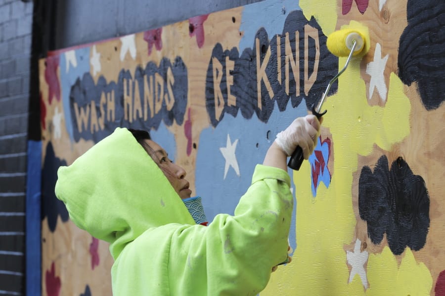 Momo Nikaido paints a mural that reads &quot;wash hands, be kind,&quot; Wednesday, April 1, 2020, on boards over windows of the Capitol Lounge, which is owned by her father in Seattle&#039;s Capitol Hill neighborhood. Most stores and businesses in the area are closed or only offering take-out food as a result of the outbreak of the new coronavirus, and state-wide stay-at-home orders from government officials. (AP Photo/Ted S.