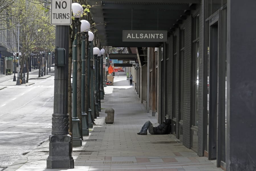A person sleeps on the sidewalk near a closed AllSaints clothing store, Saturday, April 18, 2020, in downtown Seattle. Streets remained mostly empty due to Washington state&#039;s ongoing stay-at-home order and non-essential businesses continuing to be closed as a result of the outbreak of the coronavirus. (AP Photo/Ted S.