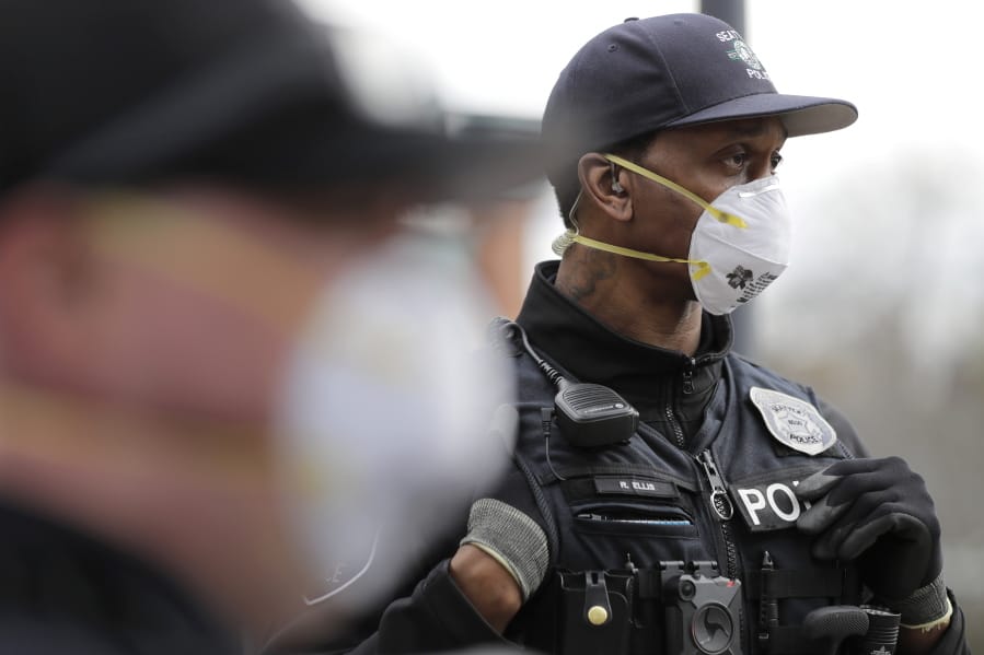 Seattle Police officer Rosell Ellis, right, wears an N95 mask as he listens to conversation during a routine call Thursday, April 2, 2020, in Seattle. As police and fire departments across the country face personnel shortages due to the spread of the new coronavirus, masks and other protective gear are being used to keep officers and firefighters still on the streets safe and healthy. (AP Photo/Ted S.
