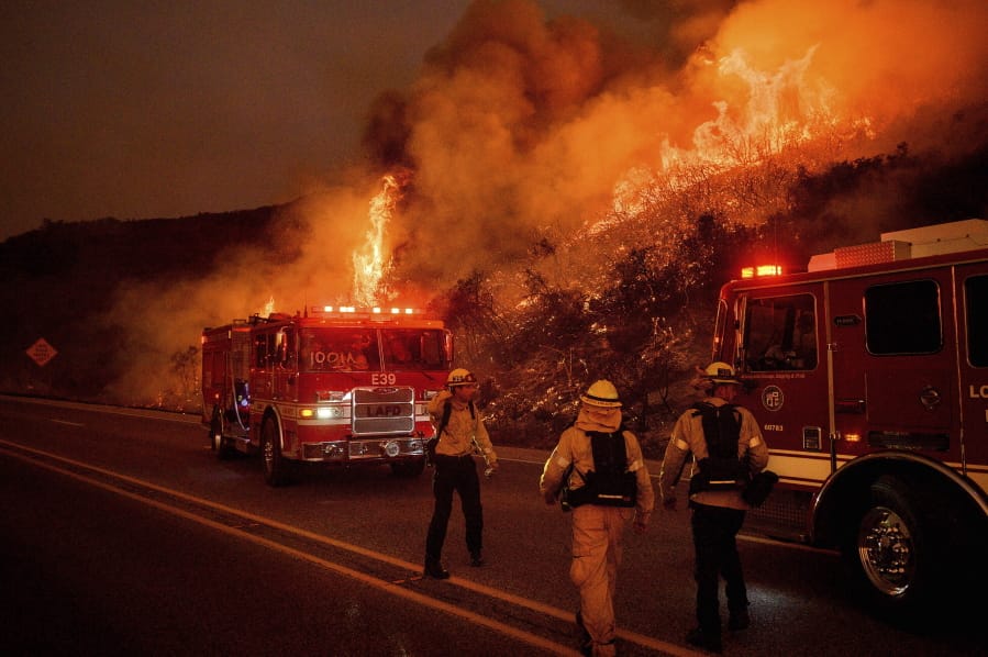 FILE - In this Nov. 26, 2019, file photo, firefighters battle the Cave Fire as it flares up along Highway 154 in the Los Padres National Forest above Santa Barbara, Calif. The outbreak of the coronavirus is making the U.S. Forest Service and others change strategies for fighting wildfires, as the need for isolation and social distancing comes into play against the necessity of having firefighters work and live closely together.