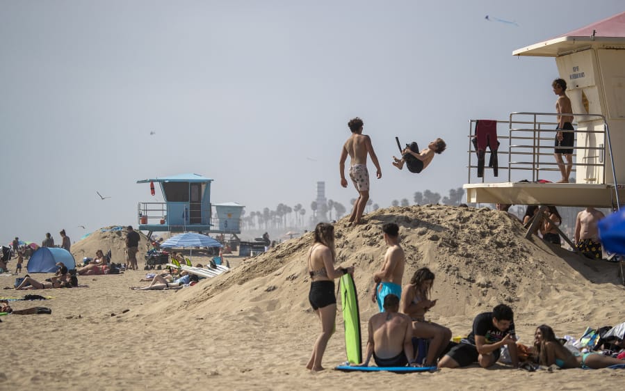 Kids do flips off the lifeguard tower while others relax on the sand on the last day of open beaches in Huntington Beach, Calif., after Gov. Newsom announced the closure of all Orange County state and local beaches, on April 30, 2020. As summer descends on the U.S., public health experts are warning that the coronavirus could make intense heat waves deadlier. (Allen J.