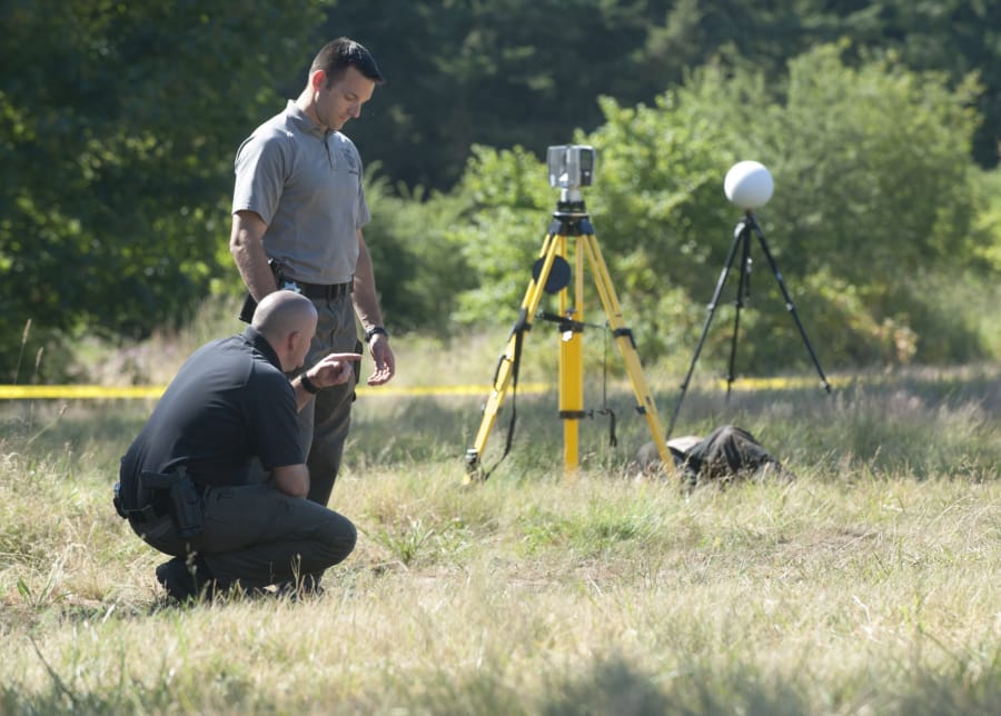 Detectives Joe Swenson, left, and Scott Gilberti investigae at the scene of a homocide in Ridgefield Wednesday July 1, 2015. The body of a man was dumped in a field off 179st Street in Ridgefield.
