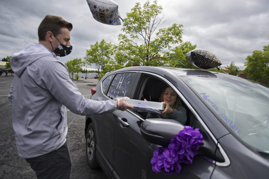 Camas High School girls basketball coach Scott Thompson, left, who owns a local cap-and-gown business that serves many Clark County high schools, gives senior Hannah Alhilali, 17, her cap and gown at Heritage High School on May 13.