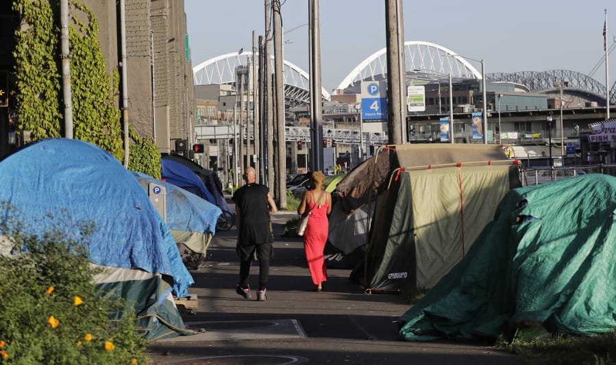 Tents used by homeless people are shown on either side of a sidewalk in Seattle with CenturyLink and Safeco Fields in the background in May 2018.  Those who work in homeless services in Seattle have found their already challenging jobs are even more taxing due to the new coronavirus pandemic. (AP Photo/Ted S.