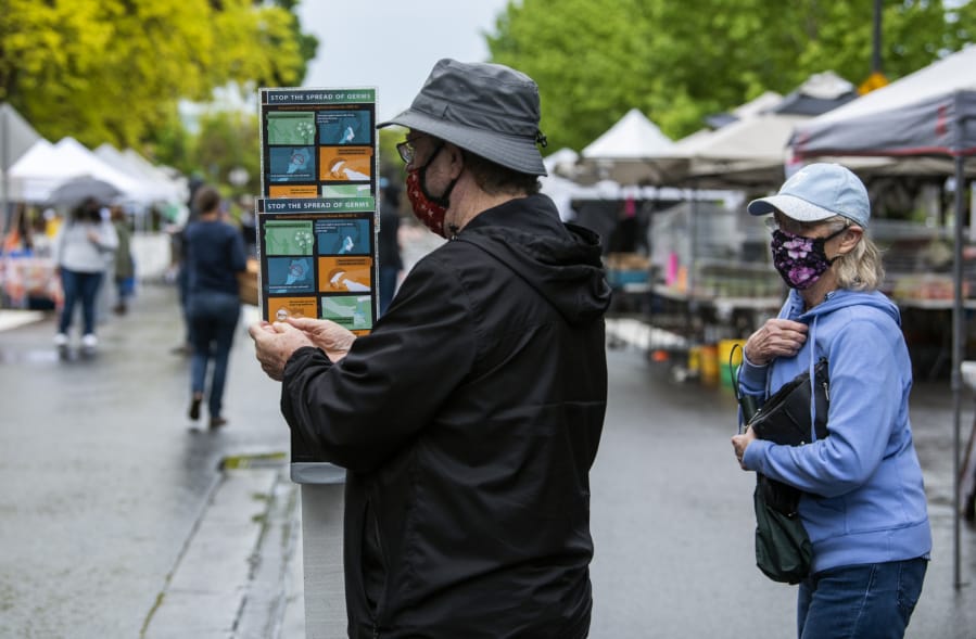 Ken Buck and his wife, Sue, use the hand sanitizer from a station in the middle of the Farmers Market in Vancouver. The re-opened market includes strict social distancing rules aimed at combating the spread of COVID-19.