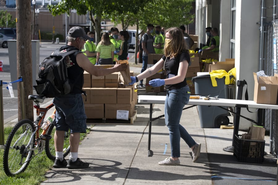 Volunteer Carlie Shoup, right, hands a sack lunch to a passerby at the FISH Westside Food Pantry in downtown Vancouver on Saturday morning. Most clients drove up and had food boxes and bags placed directly into the trunks of their cars, with no social contact necessary.