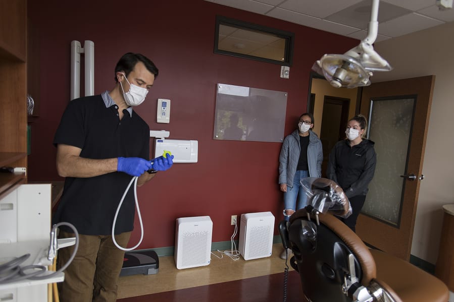 Justin Hollar, from left, of Oral Surgery Solutions in Vancouver demonstrates a new aerosol evacuator used in surgical procedures such as dental anesthesia, while assistant Elisa Spolar and oral surgery assistant Stephanie Biegler look on. Oral Surgery Solutions will operate at half its capacity for the time being to protect patients and staff from the novel coronavirus.