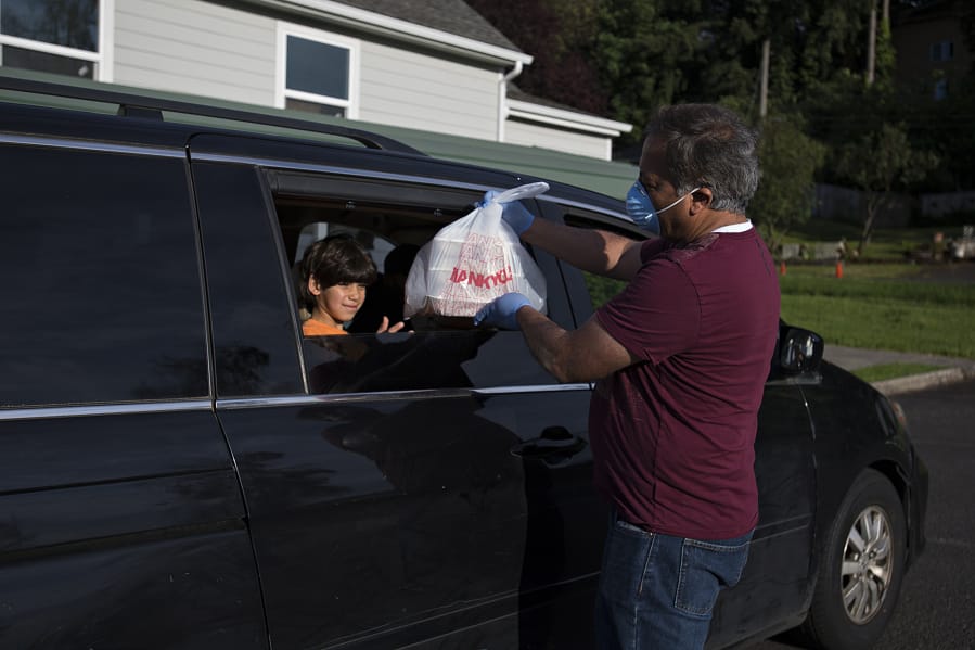 Abdullah Hariri, 7, left, helps collect meals for his family from treasurer Ahmad Qayoumi at the Islamic Society of Southwest Washington on Sunday evening. The local mosque is giving out to-go meals for Ramadan this year because of concerns about COVID-19.
