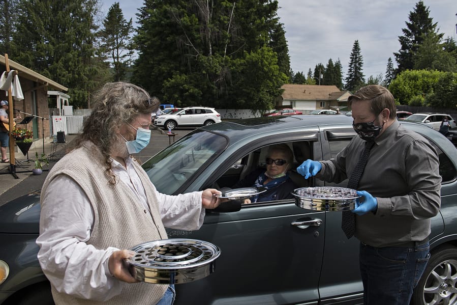 Charlie Raetz, from left, a longtime member of St. Matthew Lutheran Church in Washougal, offers communion to Camas resident Tanya Fritz with the help of Pastor Robert Barber on Sunday morning. St. Matthew Lutheran Church, a small church in Washougal, offered its first drive-in church service that also included music, a message and cookies to-go for those in attendance.