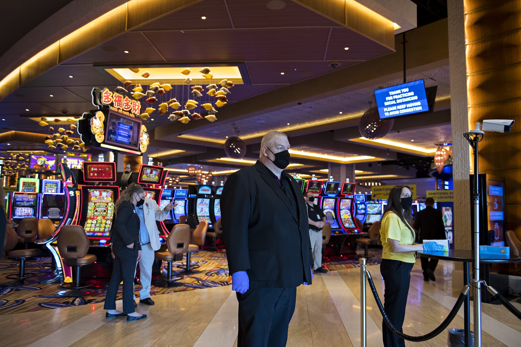 Security officer Stephen Henderson, center, wears a mask and gloves as he keeps an eye on the reopening while a thermometer, right, measures the temperature of guests at ilani Casino Resort on Thursday morning, May 28, 2020.