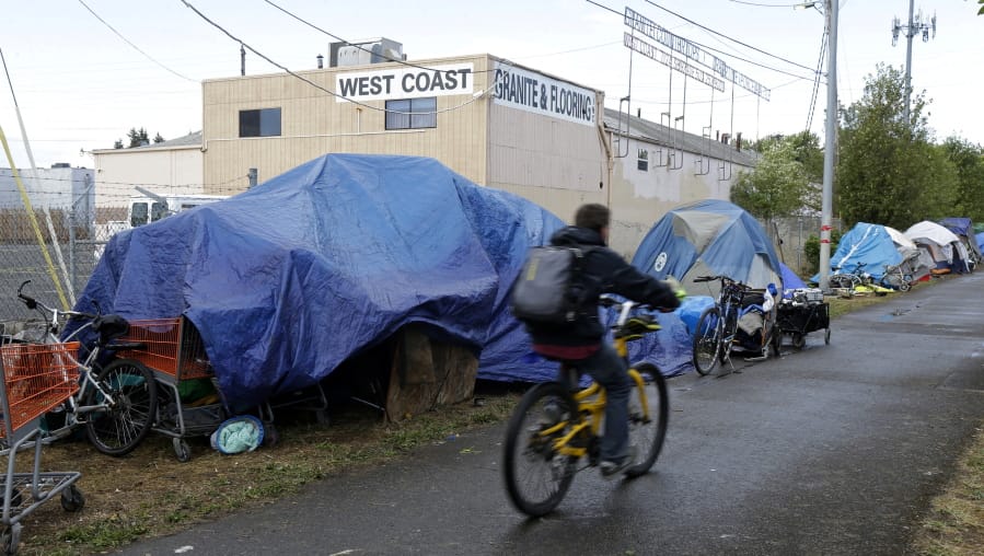 FILE - In this Sept. 19, 2017, photo, a person cycles past tents set up along a pathway in Portland, Ore. Voters in Portland will be asked Tuesday, May 19, 2020 to approve taxes on personal income and business profits that would raise $2.5 billion over a decade to fight homelessness even as Oregon grapples with the coronavirus pandemic and its worst recession in decades. (AP Photo/Ted S.