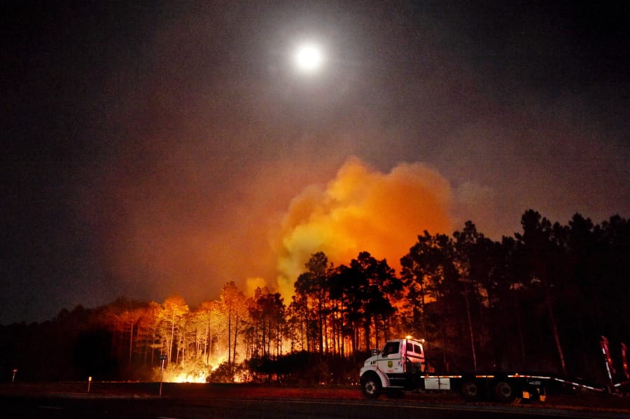 In this Wednesday evening, May 6, 2020 photo, a Florida forestry tractor trailer is parked in Walton County, Fla., near a hot spot from a wildfire. Authorities say firefighters in the Florida Panhandle battled wildfires through the night that have forced hundreds of people to evacuate from their homes. The more than 575-acre fire in Walton County prompted about 500 people to evacuate.