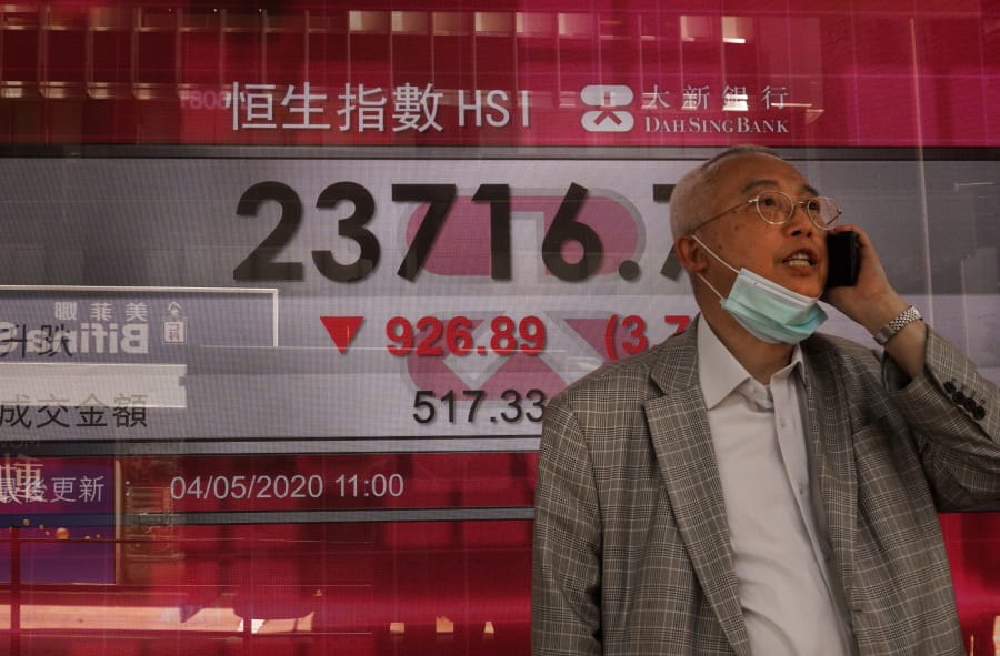 A man wearing face mask walks past a bank electronic board showing the Hong Kong share index at Hong Kong Stock Exchange Monday, May 4, 2020. Shares have skidded in Asia as tensions between the Trump administration and China over the origins and handling of the coronavirus pandemic rattle investors.