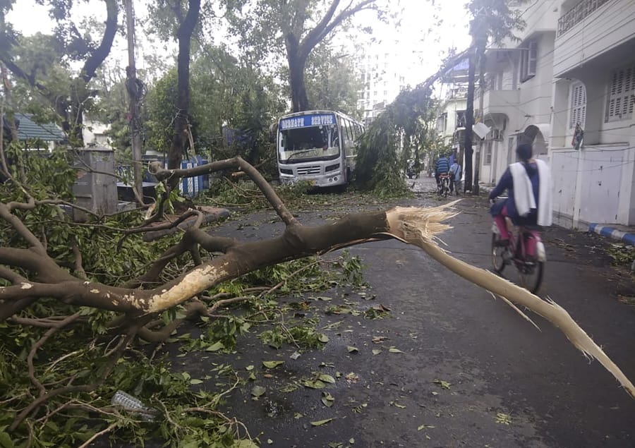 A girl rides a cycle past tree branches that fell after cyclone Amphan hit the region, in Kolkata, India, Thursday, May 21, 2020. A powerful cyclone that slammed into coastal India and Bangladesh has left damage difficult to assess Thursday.