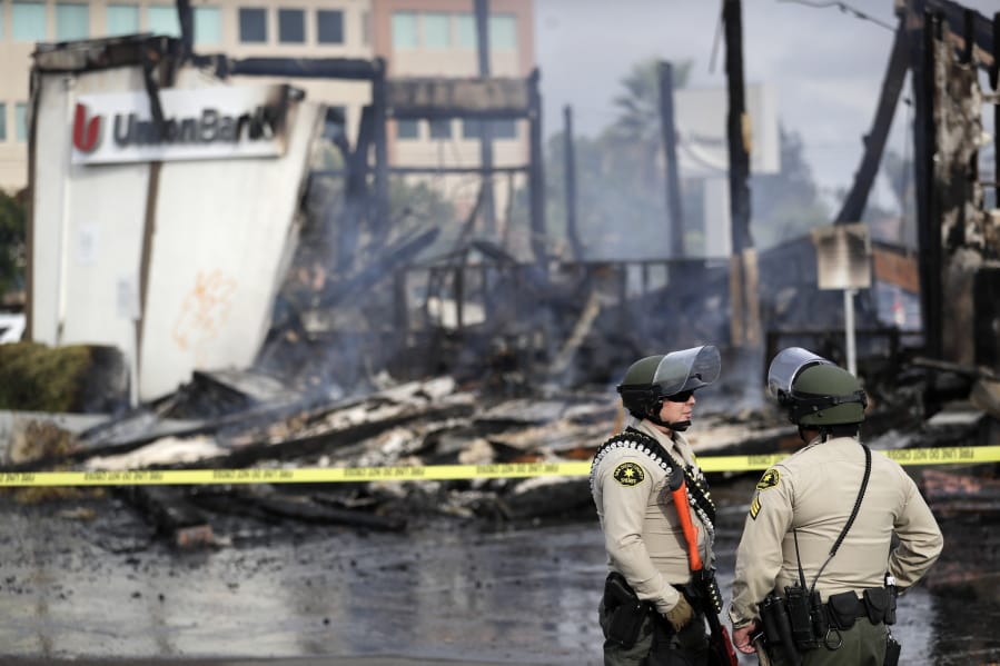 San Diego County sheriff officers stand guard in front of a burning bank building after a protest over the death of George Floyd, Sunday, May 31, 2020, in La Mesa, Calif. Protests were held in U.S. cities over the death of Floyd, a black man who died after being restrained by Minneapolis police officers on May 25.