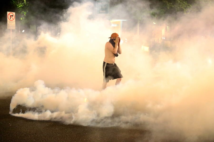A protestor covers his face as teargas envelops him in Portland, Friday, March 29, 2020.