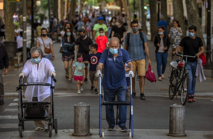 People walk on a street in Barcelona on Monday, May 25, 2020. Roughly half of the population, including residents in the biggest cities of Madrid and Barcelona, are entering phase 1 on Monday, which allows social gatherings in limited numbers, restaurant and bar service with outdoor sitting and some cultural and sports activities.