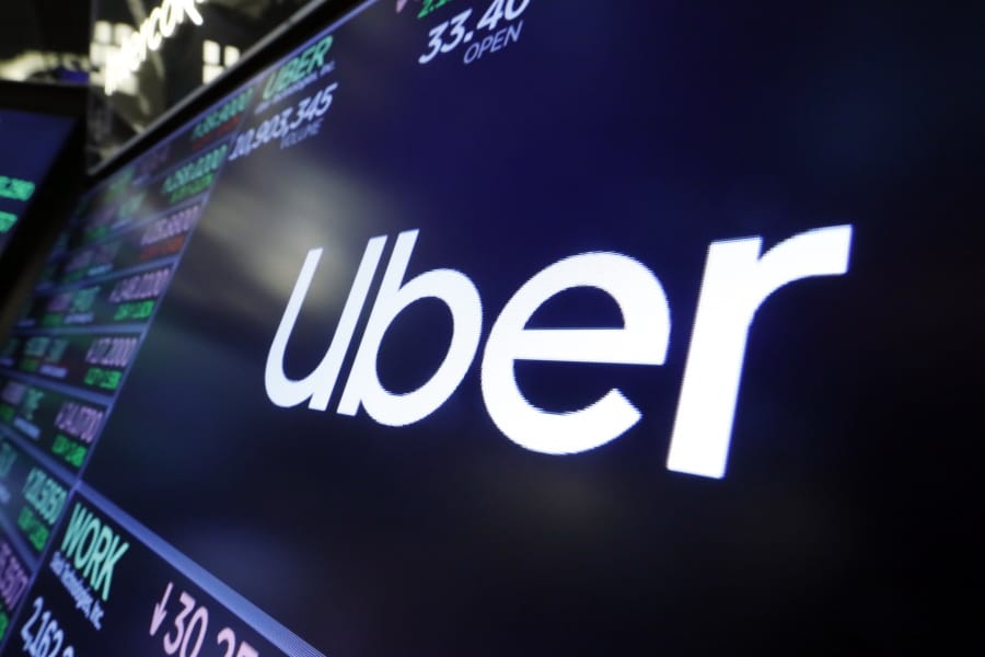 FILE - In this Aug. 16, 2019 file photo, the logo for Uber appears above a trading post on the floor of the New York Stock Exchange. Uber has cut 3,000 jobs from its workforce, its second major wave of layoffs in two weeks as the coronavirus slashed demand for rides.