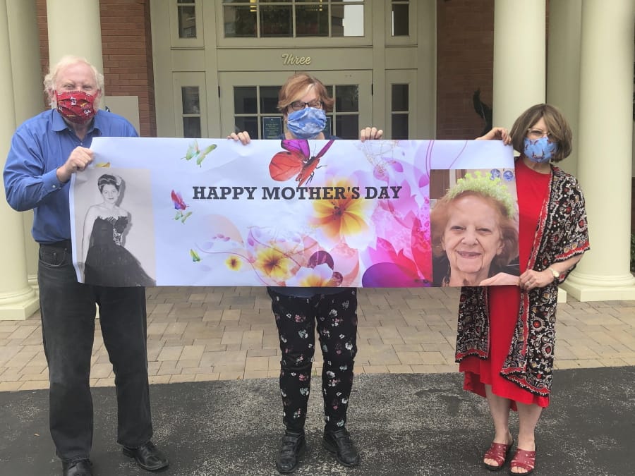 Steve Turner, from left, and his sisters, Carla Paull and Lisa Fishman, hold up a Mother&#039;s Day banner emblazoned with images of their mom, Beverly Turner, on Sunday in front of her assisted living facility in Ladue, Mo.