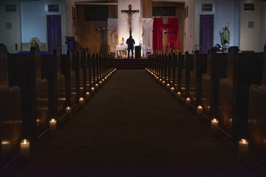A person films Pastor Nicolas Sanchez, center left, celebrating Easter Vigil Mass at his church decorated with candles and pictures sent by his parishioners attached to their pews on April 11 at St. Patrick Church in North Hollywood, Calif.