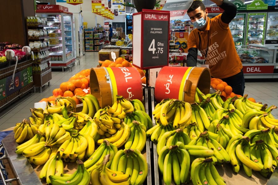 In this April 19, 2020 photo, a worker organizes bananas at a Carrefour supermarket while wearing a face mask amid the coronavirus pandemic, in Dubai, United Arab Emirates. The coronavirus pandemic has exposed just how vital foreigners are to the Gulf Arab countries where they work as medics, drivers, grocers and cleaners.