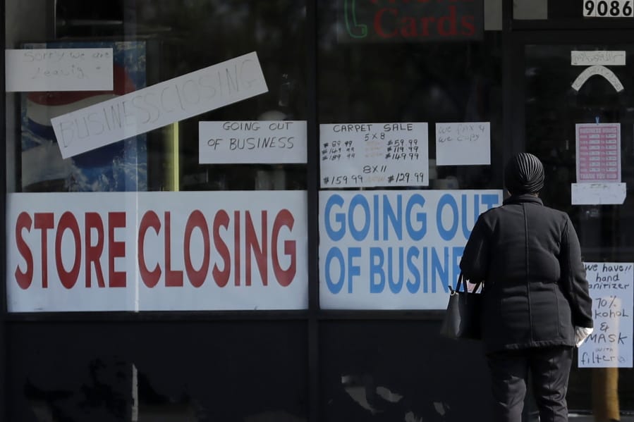 A woman looks at signs at a store closed due to COVID-19 in Niles, Ill., Wednesday, May 13, 2020. (AP Photo/Nam Y.