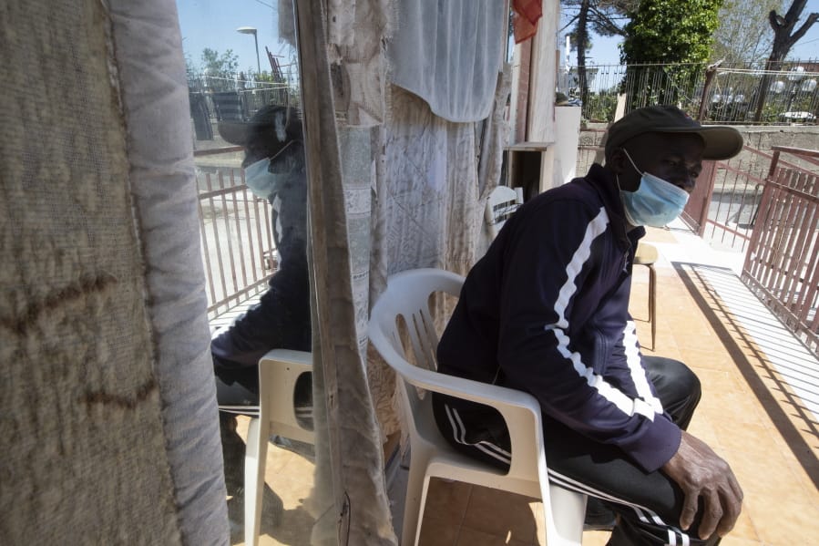 In this photo taken on Monday, April 27, 2020, a man sits outside an house where 46 men, from Nigeria and Ghana live in Castel Volturno, near Naples, Southern Italy. The house has no running water, the dilapidated electrical system doesn&#039;t reach many rooms that are in the dark. They are known as &quot;the invisibles,&quot; the undocumented African migrants who, even before the coronavirus outbreak plunged Italy into crisis, barely scraped by as day laborers, prostitutes and seasonal farm hands. Locked down for two months in their overcrowded apartments, their hand-to-mouth existence has grown even more precarious with no work, no food and no hope.