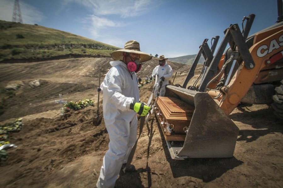 In this May 5, 2020 photo, workers in full protection gear as a precaution against the new coronavirus, unload a coffin that contain the remains of a person who died from the new coronavirus, in an area of the municipal cemetery set apart for victims of COVID-19, in Tijuana, Mexico. Citing a threat of the virus from Mexico, the Trump administration has banned hundreds of thousands of people from crossing the southern border with emergency measures that prohibit nonessential traffic and reject asylum seekers without a hearing.