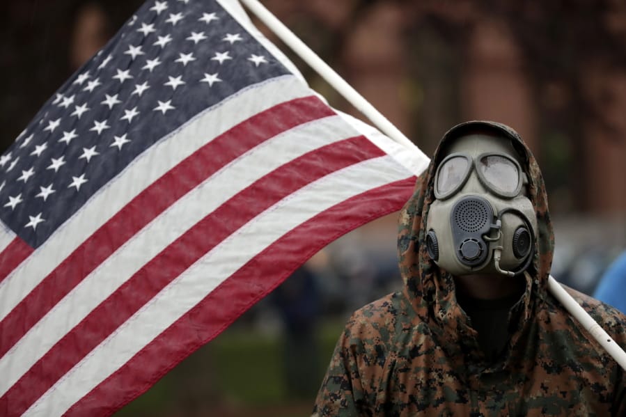 A protester wears a gas mask and carries an American flag during a rally in response to Michigan&#039;s coronavirus stay-at-home order at the State Capitol in Lansing, Mich., Thursday, May 14, 2020.
